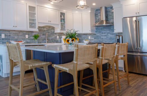 Kitchen with white cabinets, stainless steel appliances, navy island, white counters, wicker bar stools, and hardwood flooring