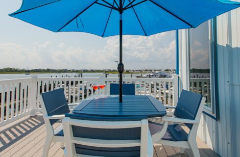 Outdoor patio with navy blue and white patio table and chairs and blue umbrella overlooking the marina