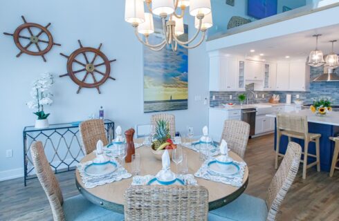 Dining room with vaulted ceiling, white walls, hardwood flooring, round wooden table, wicker chairs, and view of open kitchen