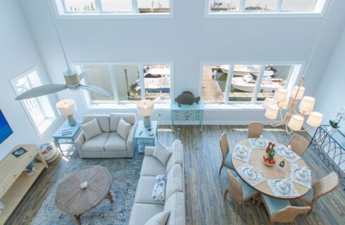 View of living room and dining room from loft area with white walls, vaulted ceiling, hardwood flooring, and view of the marina outside