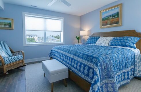 Bedroom with light blue walls, hardwood flooring, wooden bed, blue bedding, wooden wicker rocking chair, and wooden dresser