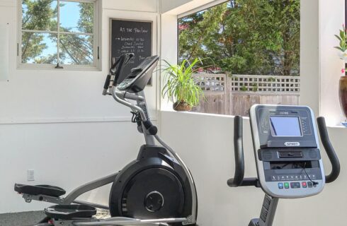 Workout room with exercise equipment and open windows to the backyard pool