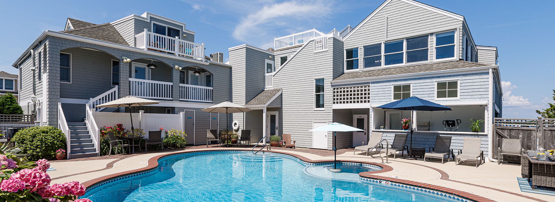 Exterior view of lodging property with gray cedar shake siding, white trim, pool, hot tub, and patio furniture